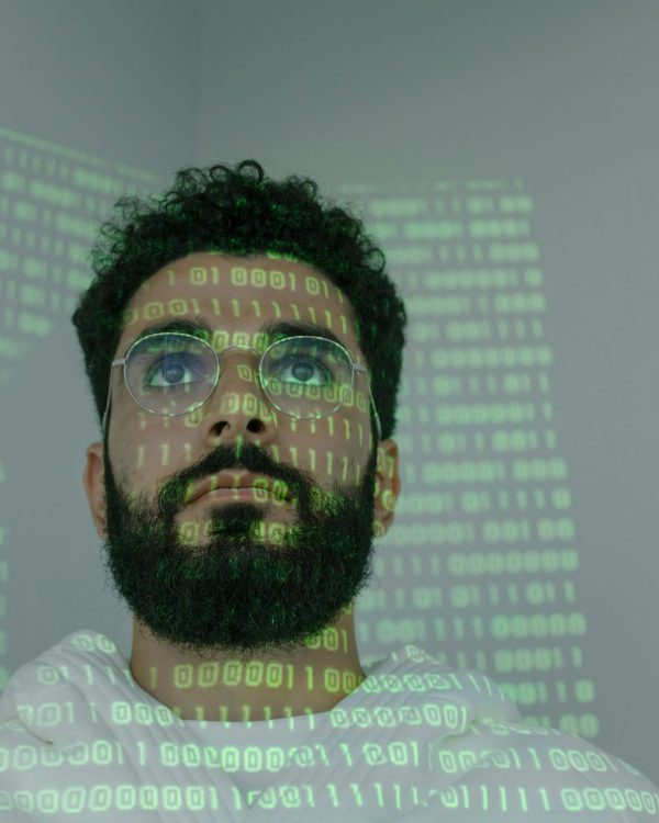 A bearded man with eyeglasses analyzing data in a digital environment with green binary code projections.